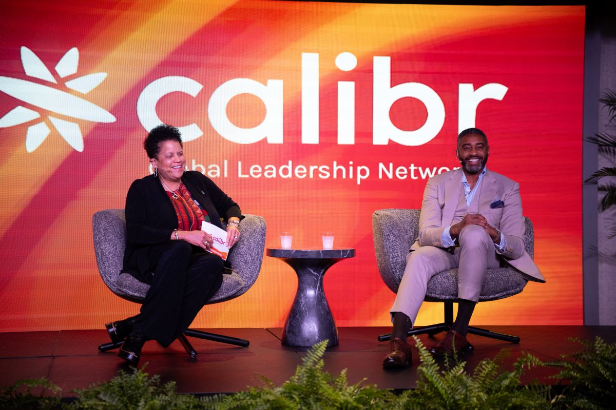 Viveca and Andre sitting in chairs on a stage in front of a calibr banner